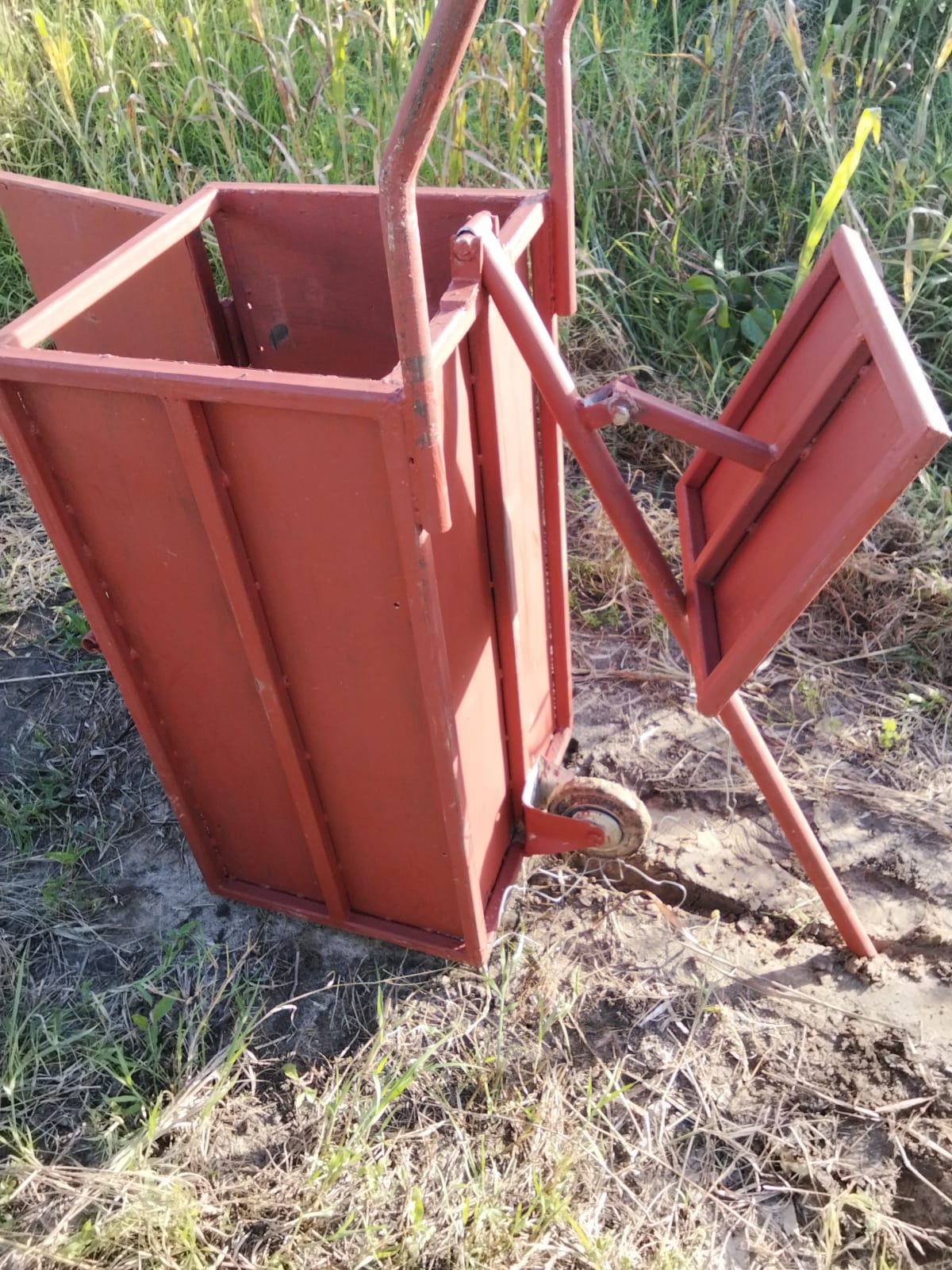 The hand baler, a red metal press that compresses cut grass into stackable bales.